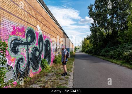 Senior man auf dem Wander- und Radweg auf der Route der ehemaligen Berliner Mauer, Baumschulenweg, Treptow-Köpenick, Berlin. Graffiti-bedeckte Wand Stockfoto