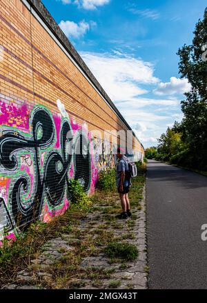 Senior man auf dem Wander- und Radweg auf der Route der ehemaligen Berliner Mauer, Baumschulenweg, Treptow-Köpenick, Berlin. Graffiti-bedeckte Wand Stockfoto