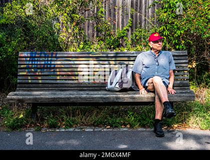 Ein älterer Mann ruht auf einer Bank neben dem Wander- und Radweg an der Route der ehemaligen Berliner Mauer, Baumschulenweg, Treptow-Köpenick, Berlin. Stockfoto