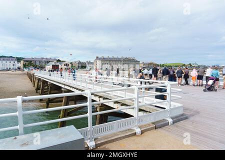 Touristen und Besucher genießen einen Sommernachmittag am Beaumaris Pier, einer beliebten Touristenattraktion am Meer auf der Insel Anglesey Wales Stockfoto