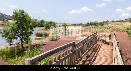 Rot gefärbter Küstensee hinterlässt tonähnliche Sedimente und hölzerne Brückenzugänge auf dem Salagou-See in Südfrankreich Stockfoto