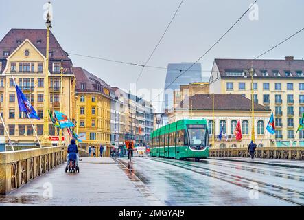 BASEL, SCHWEIZ - 1. APRIL 2022: Blick auf moderne grüne Straßenbahnfahrt auf der Mittlere Brucke an Regentagen am 1. April in Basel, Schweiz Stockfoto