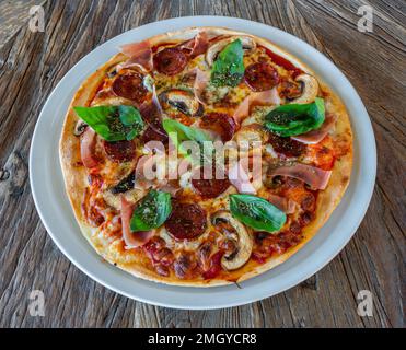 Frische Pizza mit Spinatjamon und Pilzen auf einem hölzernen Hintergrund aus nächster Nähe. Peperoni Stockfoto