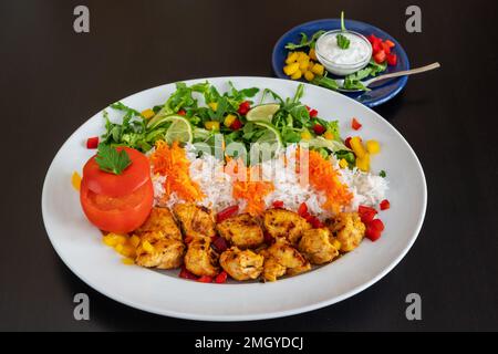 Jooje Kebab aus Kalbfleisch mit Reis, Gemüse und Sauce auf schwarzem Hintergrund. Stockfoto