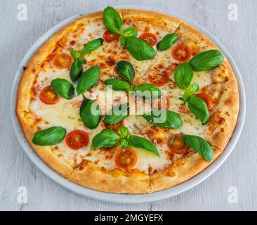 Caprese-Pizza mit Suluguni-Käse und Tomaten, mit Pesto-Sauce bedeckt. Auf einem hölzernen Hintergrund auf einem Schild. Stockfoto