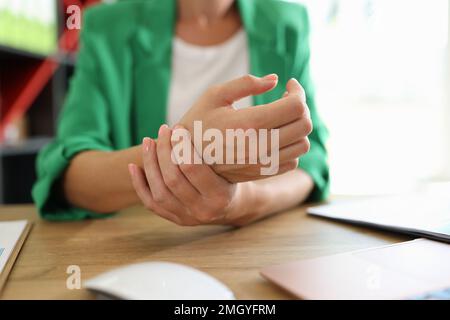 Nahaufnahme einer Managerin, die ihr schmerzhaftes Handgelenk hält, verursacht durch lange Büroarbeit. Stockfoto