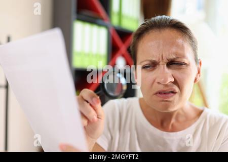 Unzüchtige Frau mittleren Alters, die durch eine Lupe auf den Dokumenttrog blickt. Stockfoto