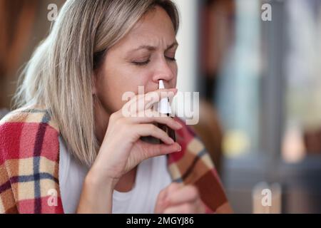 Frau mit Krankheit, mit Decke bedeckt, benutzt Nasenspray Nahaufnahme. Stockfoto