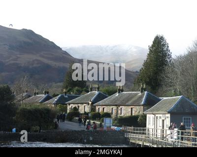 Reihen von Steinhäusern säumen die Pier Road im Naturschutzdorf Luss am Ufer des Loch Lomond mit einer spektakulären Bergkulisse. Stockfoto