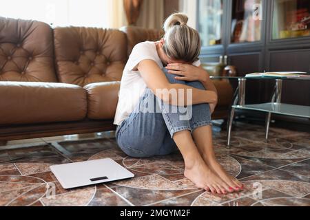 Traurige Frau sitzt auf dem Boden neben Schuppen und hält ihre Knie mit den Händen. Stockfoto