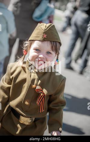 9. Mai 2015, Kolomna, Moskau, Russland. Feier zum Siegesfeiertag. Porträt eines Kindes in Militäruniform mit Blumen am 9. Mai. Eine lächelnde Polizistin Stockfoto