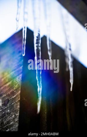 Eiszapfen auf dem Dach schmelzen in Regenbogenlicht, hergestellt von Prism im Winter Stockfoto