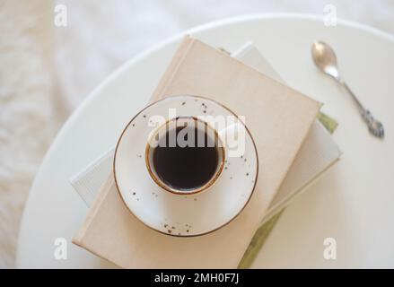 Eine Tasse schwarzen Kaffees steht auf einem Stapel Bücher auf dem Tisch Stockfoto