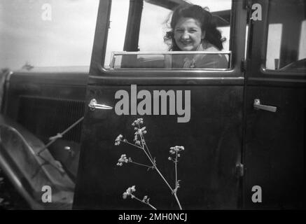 Etwa Ende der 1940er Jahre, historisch, eine Dame, die auf dem Beifahrersitz eines Autos der Epoche sitzt und aus dem Fenster blickt, das heruntergeklappt ist, England, Großbritannien. In dieser Zeit war der Autohersteller in Großbritannien gering, und es war ein großer Anlass, einen Tag auf dem Land zu verbringen. Die Tür ist mit Scharnieren nach hinten befestigt, was bei Autos dieser Zeit üblich ist. Stockfoto