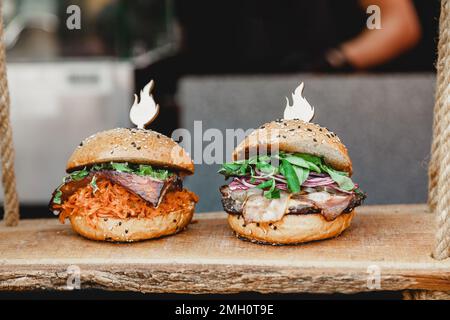 Leckere Burger auf Holzbasis. Zwei leckere hausgemachte Burger mit Rindfleisch, Käse und Gemüse auf einem alten Holztisch. Fett ungesunde Lebensmittel Nahaufnahme Stockfoto