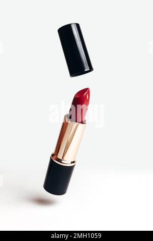 Roter Lippenstift mit geöffnetem Deckel in goldener und schwarzer Tube, Kosmetik, Schweben, auf weißem Hintergrund Stockfoto