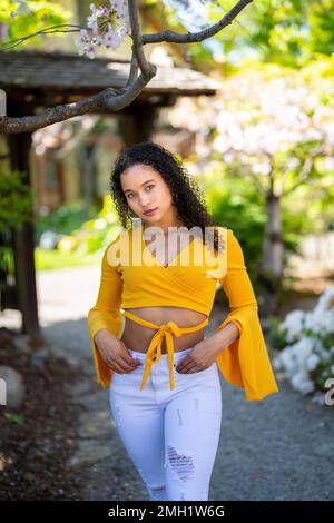 Nach vorne gerichtetes 3/4-Körperporträt einer jungen afroamerikanischen Frau, die im japanischen Garten im Frühling auf dem Dirt Path steht Stockfoto