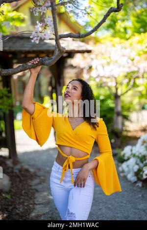 Nach vorne gerichtetes 3/4-Körperporträt einer jungen afroamerikanischen Frau, die im japanischen Garten im Frühling auf dem Dirt Path steht Stockfoto