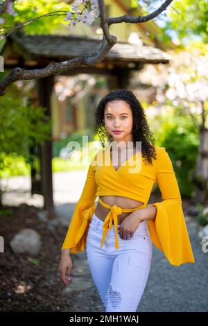 Nach vorne gerichtetes 3/4-Körperporträt einer jungen afroamerikanischen Frau, die im japanischen Garten im Frühling auf dem Dirt Path steht Stockfoto