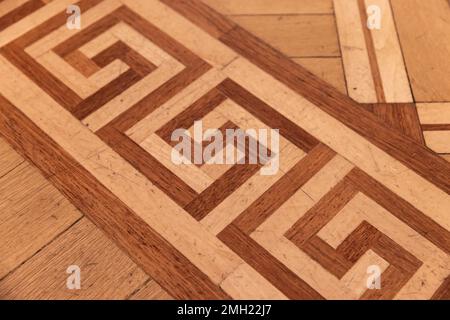 Altmodisches Parkett aus verschiedenen Holzplanken mit geometrischen Verzierungen, bekannt als der griechische Schlüssel oder Meander. Fotostruktur des Hintergrunds Stockfoto