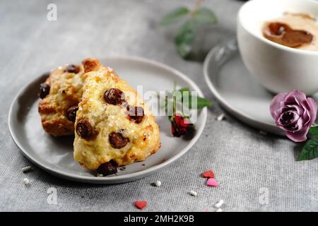 Frühstücksraum am Valentinstag - Scones Cappuccino Herz und Rosen auf einem Tablett, selektiver Fokus Stockfoto