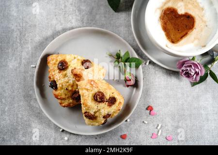 Frühstücksraum am Valentinstag - Scones Cappuccino Herz und Rosen auf einem Tablett, selektiver Fokus Stockfoto