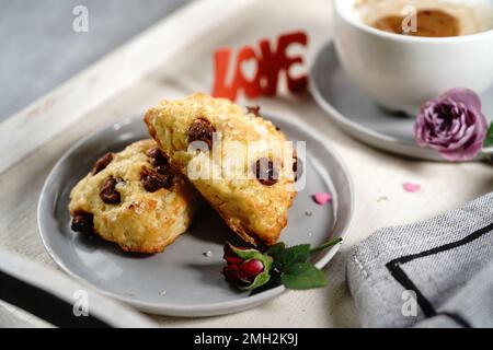 Frühstücksraum am Valentinstag - Scones Cappuccino Herz und Rosen auf einem Tablett, selektiver Fokus Stockfoto