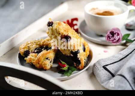 Frühstücksraum am Valentinstag - Scones Cappuccino Herz und Rosen auf einem Tablett, selektiver Fokus Stockfoto