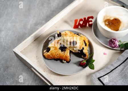 Frühstücksraum am Valentinstag - Scones Cappuccino Herz und Rosen auf einem Tablett, selektiver Fokus Stockfoto