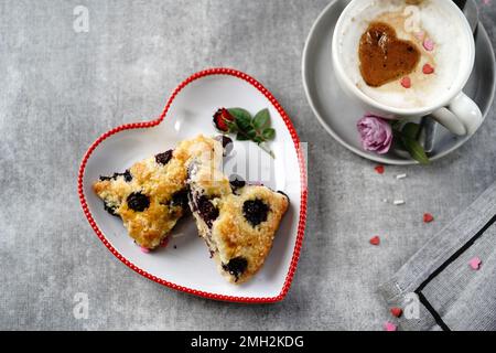 Frühstücksraum am Valentinstag - Scones Cappuccino Herz und Rosen auf einem Tablett, selektiver Fokus Stockfoto