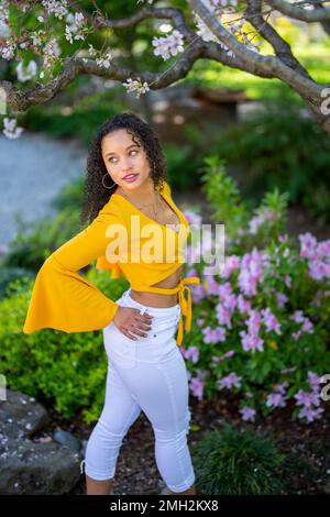 Down-Angle-Porträt einer glücklichen jungen afroamerikanischen Frau in einem blühenden Garten im japanischen Stil im Frühling Stockfoto