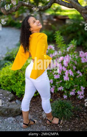 Down-Angle-Porträt einer glücklichen jungen afroamerikanischen Frau in einem blühenden Garten im japanischen Stil im Frühling Stockfoto