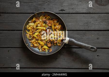 Gedünstete Paprika mit Pilzen und Zwiebeln in einer Bratpfanne auf einem schwarzen Holztisch, gedünstetes Gemüse in einer Bratpfanne Stockfoto