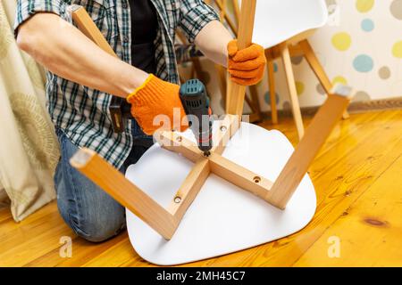 Möbel zusammenbauen. Der Mann, der den Stuhl zusammensetzt. Möbelbauer mit Bohrer Stockfoto