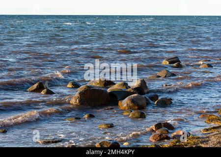 Große Steine liegen im Wasser an der Ostseeküste, mit Wellen und Horizont Stockfoto