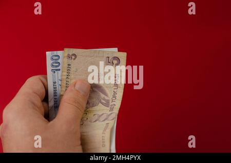 Eine Hand hält eine Banknote von 100 yuz turk lirasi auf rotem Hintergrund Stockfoto
