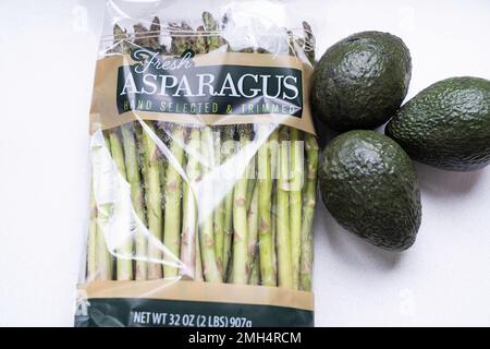 Frische Spargelspieße in einem Zellophan-Paket mit drei grünen unreifen Avocados daneben. Stockfoto
