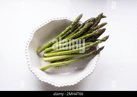 Frische rohe Spargelspitzen, Spargel officinalis, in einer weißen Schüssel auf weißem Hintergrund. Stockfoto