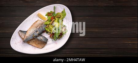 Gebackenes Makrelenfilet mit Salat und Pilzen auf einem Teller auf Holzhintergrund. Banner Stockfoto