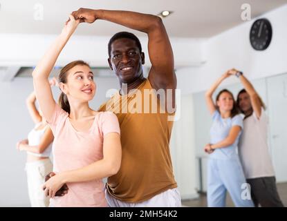 Positiv lächelndes Tanzpaar, das während des Gruppentrainings im Tanzsaal aktiv tanzt Stockfoto