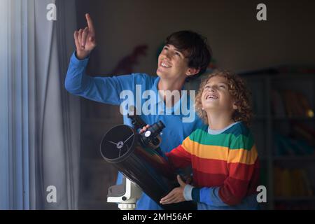 Kleiner Junge und junger Mann, der Sterne durch das Teleskop betrachtet. Kinder und Eltern beobachten Nachthimmel und Mond. Astronomiewissenschaft für Forscherkind. Stockfoto