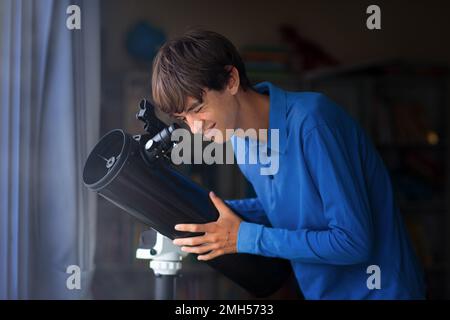 Junger Mann, der Sterne durch das Teleskop betrachtet. Ein Teenager, der den Nachthimmel beobachtet. Teenager, der Planeten und Mond beobachtet. Astronomie-Hobby. Stockfoto