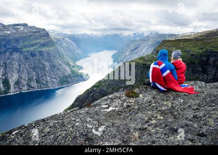 Paar sitzt auf Felsen und blickt auf die Berge in der Nähe von trolltunga. Beliebte Touristenattraktion. Ringedalsvatnet - See in der Gemeinde Odda in Hordalan Stockfoto