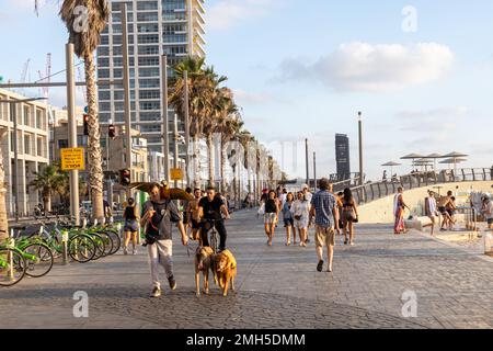 Tel Aviv, Israel - 20.07.2022, Skyline und Sandstrände von Tel Aviv bei Sonnenuntergang. Die Leute laufen entlang der Promenade am Strand entlang. Ein Mann mit einem parr Stockfoto