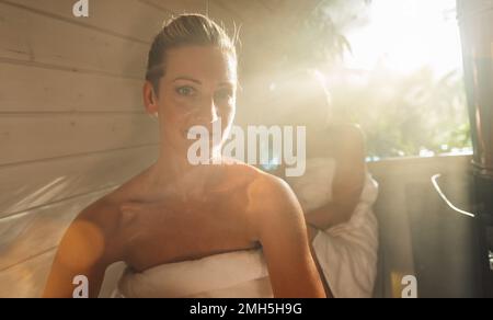 Glückliche Freundinnen, die sich in der hölzernen Fass-Sauna im Summer in norwegen entspannen. Die Leute sind entspannt und genießen den Urlaub, während sie sich in der finnischen Saun entspannen Stockfoto