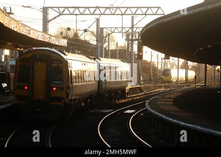 Northern Züge Express Sprinter dmu wartet am Bahnhof Carnforth am 25. Januar 2023, während Avanti West Coast pendolino an der West Coast Main Line vorbeifährt. Stockfoto