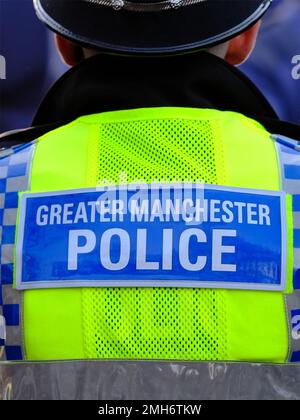 Polizist von hinten zeigt hochglänzende Weste mit den Worten "Greater Manchester Police" auf einem blauen Abzeichen Stockfoto