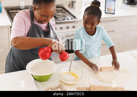 Frohe afroamerikanische Großmutter und Enkelin, die zusammen in der Küche backen Stockfoto
