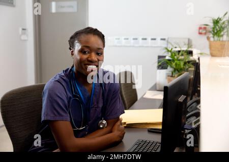 Portrait einer glücklichen afroamerikanischen Ärztin, die im Krankenhaus arbeitet, am Schreibtisch sitzt Stockfoto