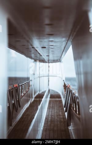 Eine vertikale Aufnahme des Mitteldecks einer Touristenjacht mit einer sehr flachen Feldtiefe und einem selektiven Fokus auf dem Holzboden und einer Gruppe gestreifter t Stockfoto